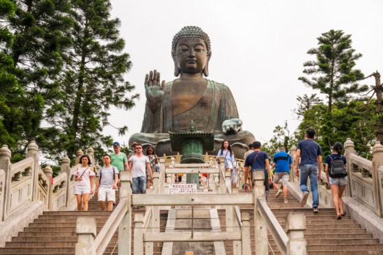 A group of diverse travelers ascending the stairs towards a giant Buddha statue, symbolizing international travel, cultural experiences, and global connection.