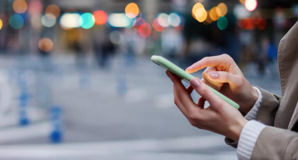 A person using a smartphone in a busy urban setting with colorful bokeh lights in the background, representing international travel and global insurance solutions.