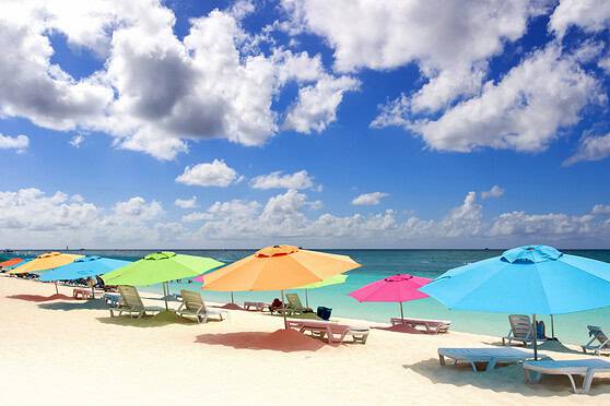 Vibrant beach scene featuring multicolored umbrellas, sun loungers, and turquoise water under a partly cloudy sky for tropical vacation insurance.