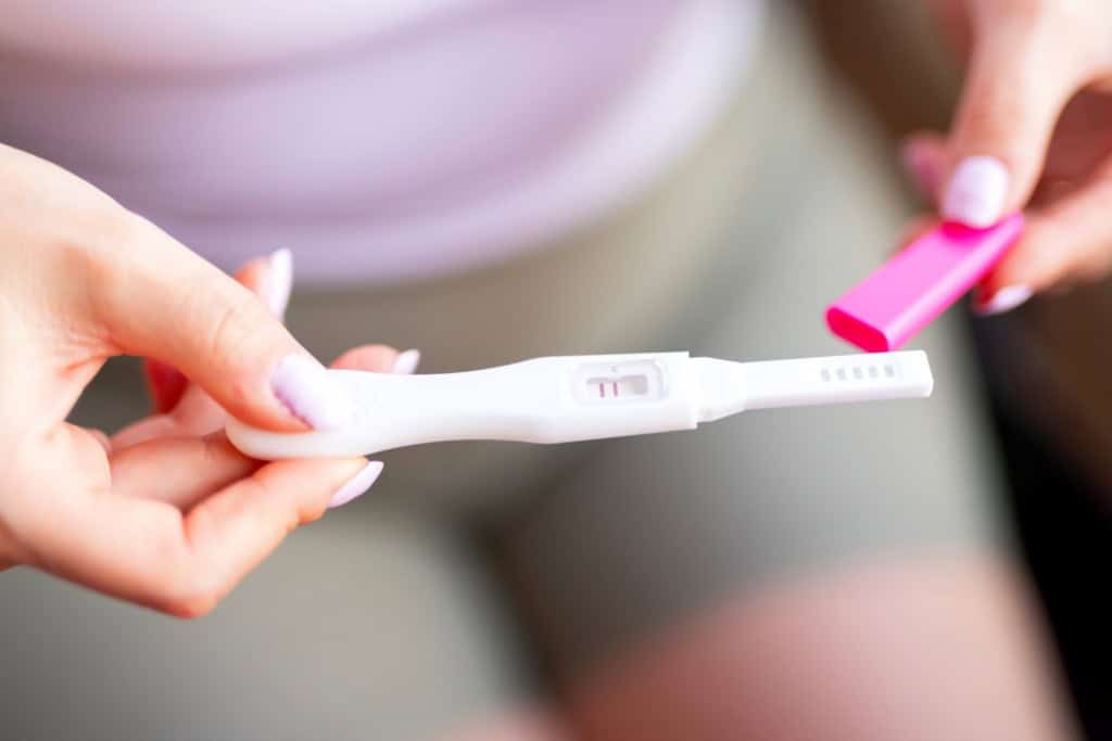 a woman holding a positive pregnancy test, knowing she will need to arrange maternity insurance