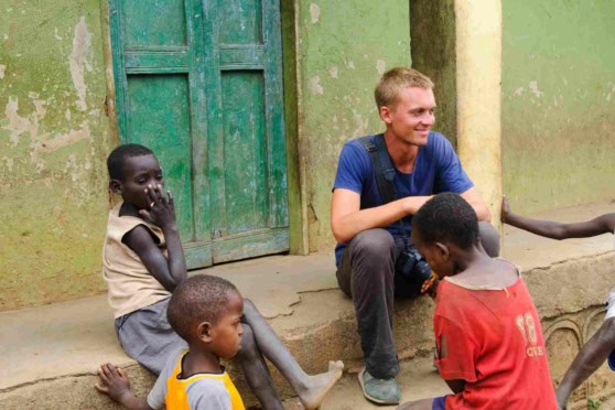 Young man visiting children in a developing country, promoting international aid and volunteer work for community development.