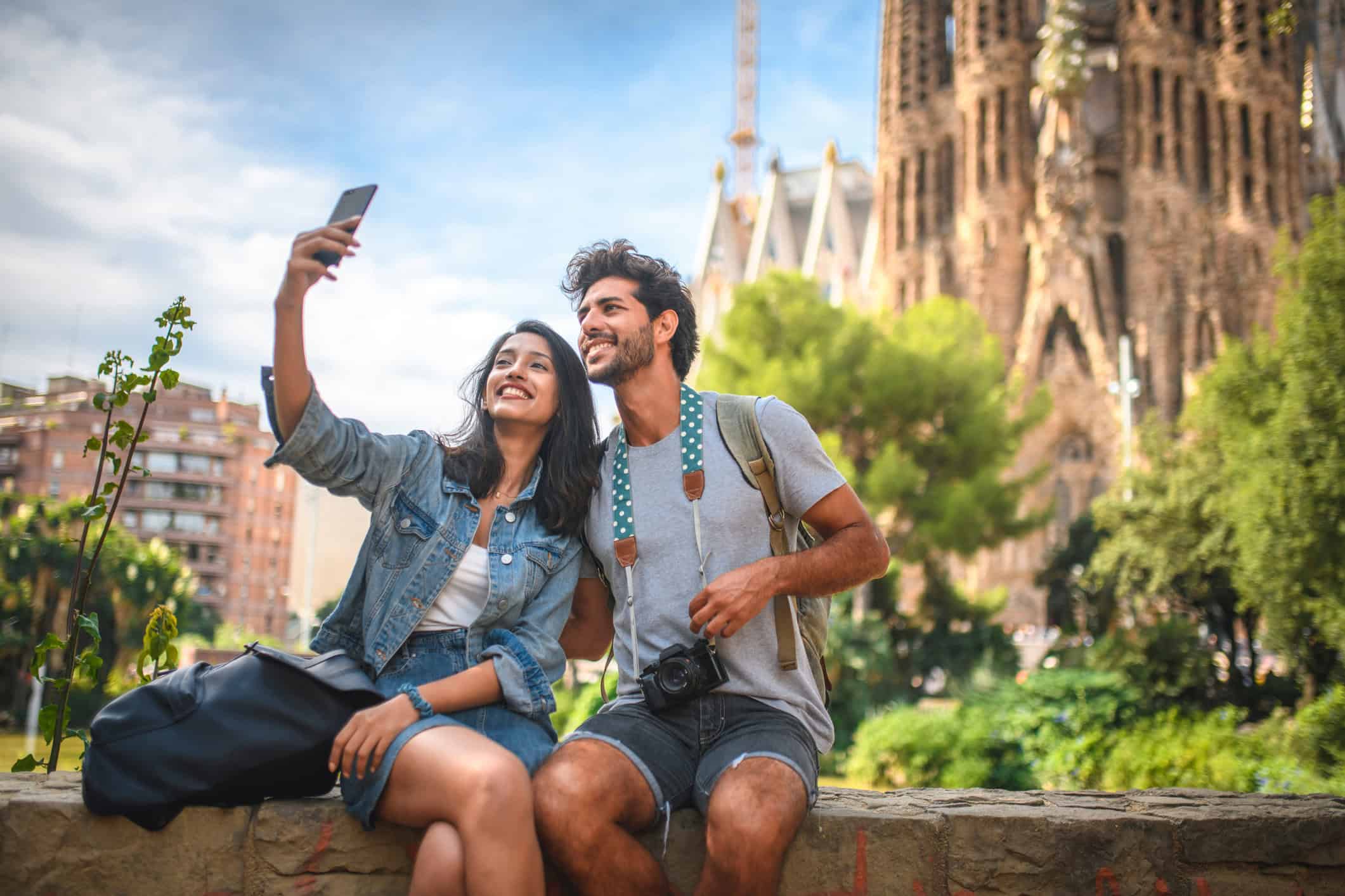 Two young travelers taking a selfie in front of Sagrada Família in Barcelona, Spain, highlighting international travel and adventure.