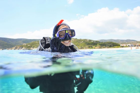 A smiling woman with scuba gear enjoying underwater adventure in a beautiful coastal location, representing international travel insurance coverage for explorers.