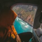 American Express travel insurance - a traveler in an orange parka takes a helicopter ride