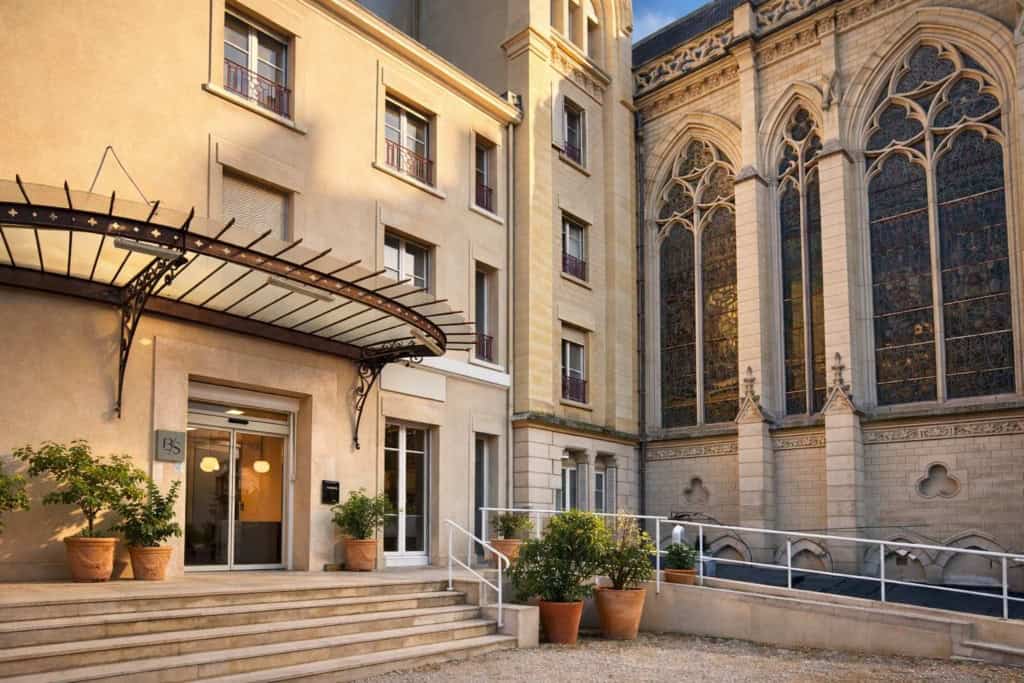Exterior of Clinique Blomet, a private hospital in central Paris, France, showing the main entrance with steps, an accessible ramp, potted plants, and an adjoining historic building with tall stained-glass windows.