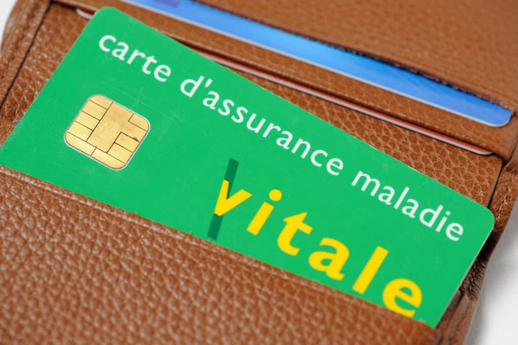 Vital health insurance card (Carte Vitale) in French, placed inside a brown leather wallet, on a page about health insurance for foreigners in France.
