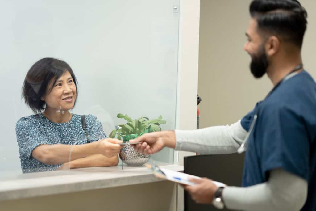 A female patient presenting a health card at a clinic reception, illustrating access to care with public health insurance in Canada.