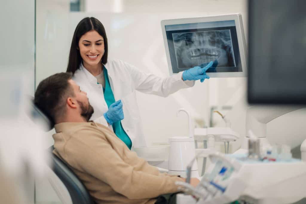 Dentist showing dental X-ray to a patient in a clinic, with focus on international health care services.
