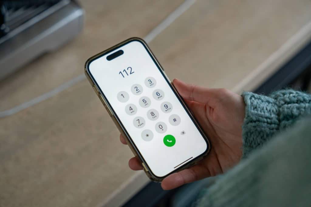 Person holding a smartphone with emergency number 112 displayed, in an international health insurance context.