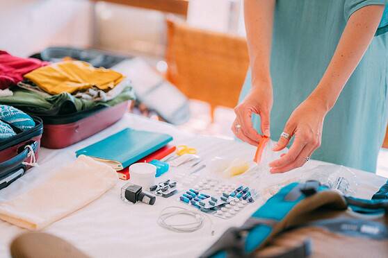 Person packing a travel medical kit with medications and supplies on a table, preparing for international relocation as part of their health checklist for moving abroad