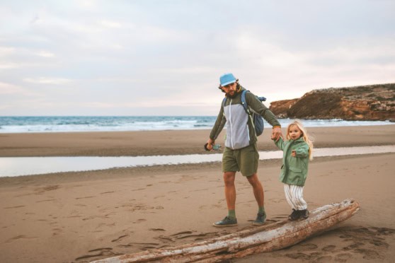 A man and child walk hand-in-hand on a beach, highlighting the need for international health insurance coverage while exploring worldwide destinations.