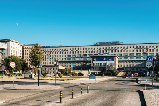 A large, contemporary office building under a clear blue sky with various traffic signs and greenery in the foreground.
