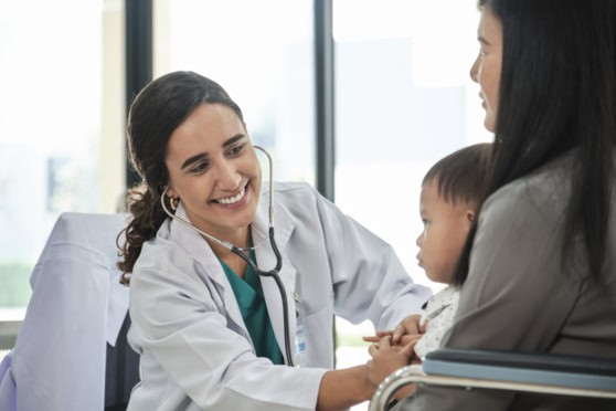 A caring doctor in a white coat uses a stethoscope to examine a young girl, comforting her mother during a pediatric check-up in a modern clinic setting.
