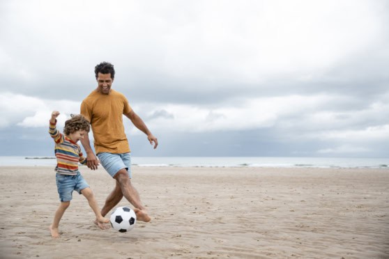 A father and son playing soccer on the sandy beach under a cloudy sky, capturing family fun, outdoor activities, and healthy lifestyle themes perfect for SEO on beach sports.