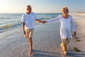 Happy senior man and woman couple walking and holding hands on a deserted tropical beach with bright clear blue sky Happy senior man and woman couple walking and holding hands on a deserted tropical beach with bright clear blue sky