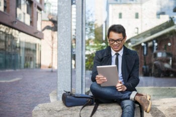 Young asian man looking at digital tablet Young smiling asian business man looking at digital tablet sitting outside on city street