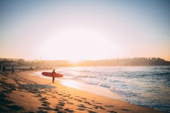 Healthcare in Australia: Man with a surfboard stands at the shore of Bondi Beach