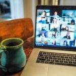 Remote working fatigue: A green pottery mug sits next to an open laptop showing many people on a video calll