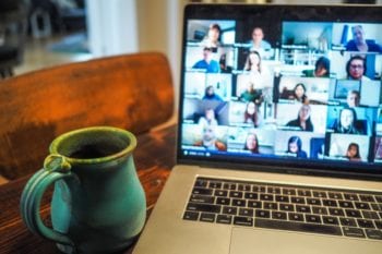 A green mug sits next to an open laptop showing people on a video call working remotely