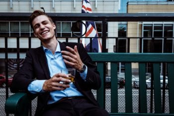 expats from UK: Young man in a suit relaxes on an outdoor patio with a beer and a British flag in the background