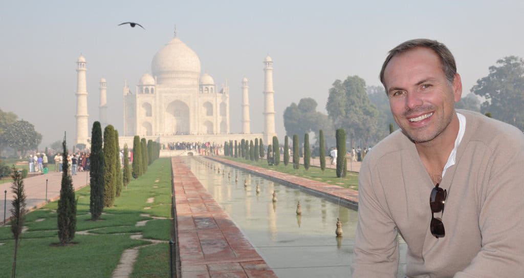 Portrait of a smiling man in front of the Taj Mahal, showcasing internationalized travel experiences and global insurance solutions for international citizens.