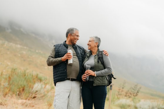A joyful, mature couple hiking in a scenic mountain landscape, smiling and sharing a moment of happiness, highlighting the importance of international travel insurance for global citizens.
