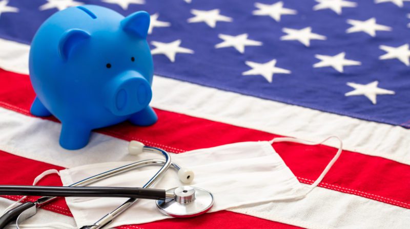 How do I save on health care costs in the USA? Piggy bank on American flag with medical gear