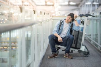 Aisan man sitting on luggage trolley, looking exhausted