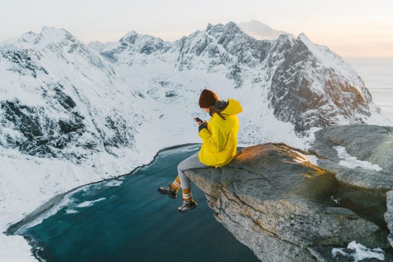 Female GeoBlue Voyager travel insurance customer sitting on a cliffs edge overlooking snowy mountains