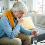 Older gray-haired man reading pill bottle