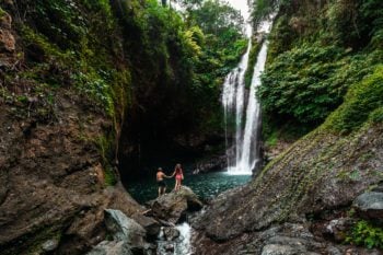 Lovers at the waterfall, rear view. Couple admiring a beautiful waterfall in Indonesia. Couple on vacation in Bali. Honeymoon trip. The couple is traveling in Asia. Vacation on the island of Bali