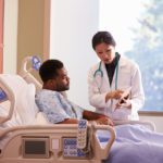 Hospital Doctor With Digital Tablet Talks To Male Patient