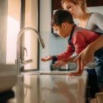 Woman helping son touch tap water, assessing drinking tap water abroad