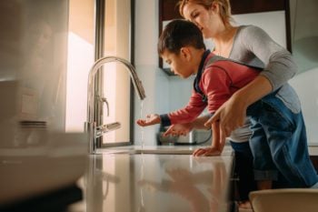 Woman helping son touch tap water, assessing drinking tap water abroad