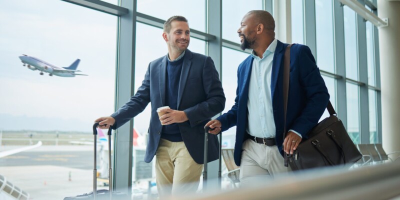 Two business men at the airport, discussing the benefits of their annual travel insurance plans.