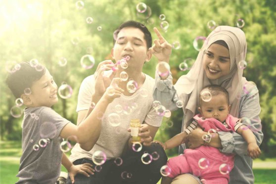 Happy family with children playing and blowing bubbles outdoors in a park setting.