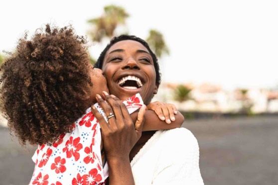 Happy woman hugging her child outdoors with a bright, joyful smile.
