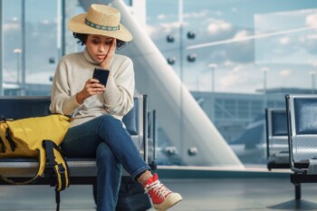 woman sitting in the airport receives news on her phone that her flight was cancelled