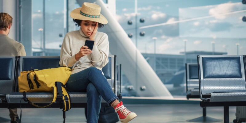 woman sitting in the airport receives news on her phone that her flight was cancelled