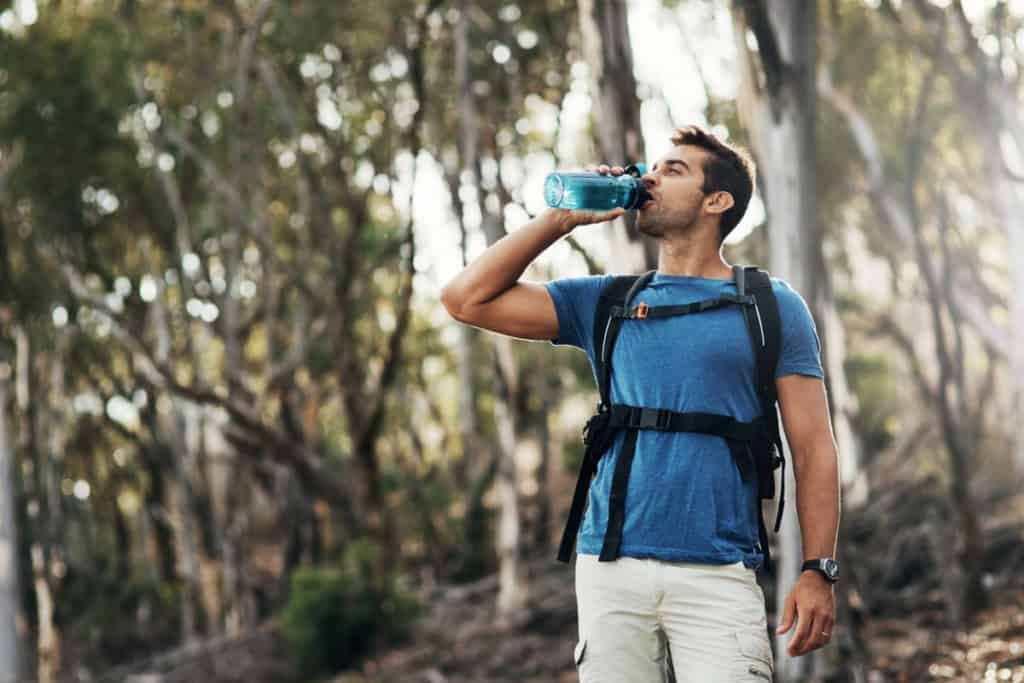 a hiker drinking water, staying hydrated while also covered by adventure travel insurance