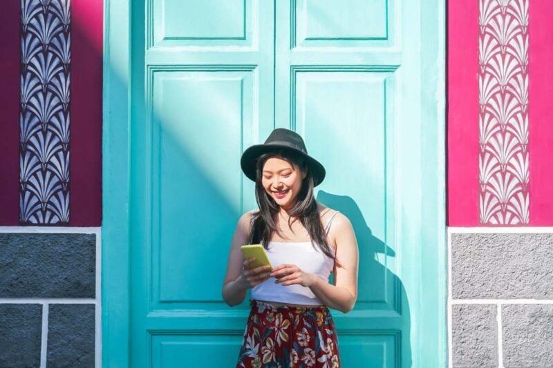 an asian girl smiling at her cell phone as she makes a call abroad using our international calling codes