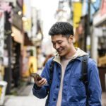 an asian man smiling at his cell phone as he makes a call abroad using our international calling codes