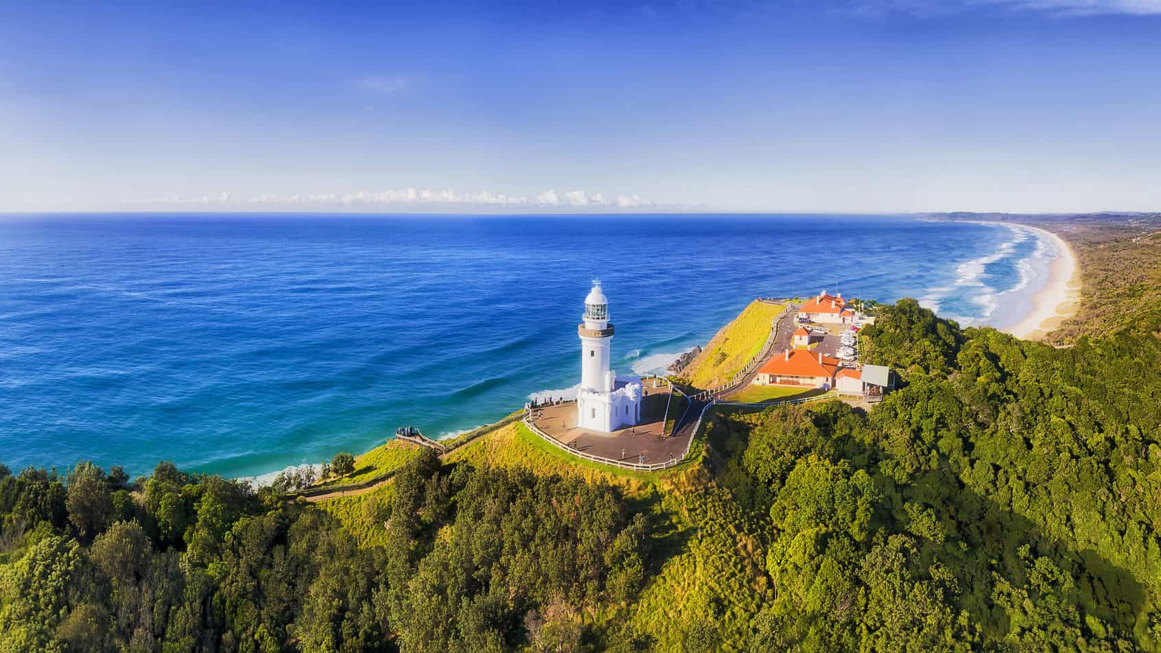 A scenic aerial view of a lighthouse on a lush green cliffside by the ocean, emphasizing international travel insurance and coverage options for expatriates and travelers worldwide.