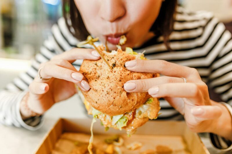 a woman biting into a burger in the United States, where life expectancy per country is lower than many European countries