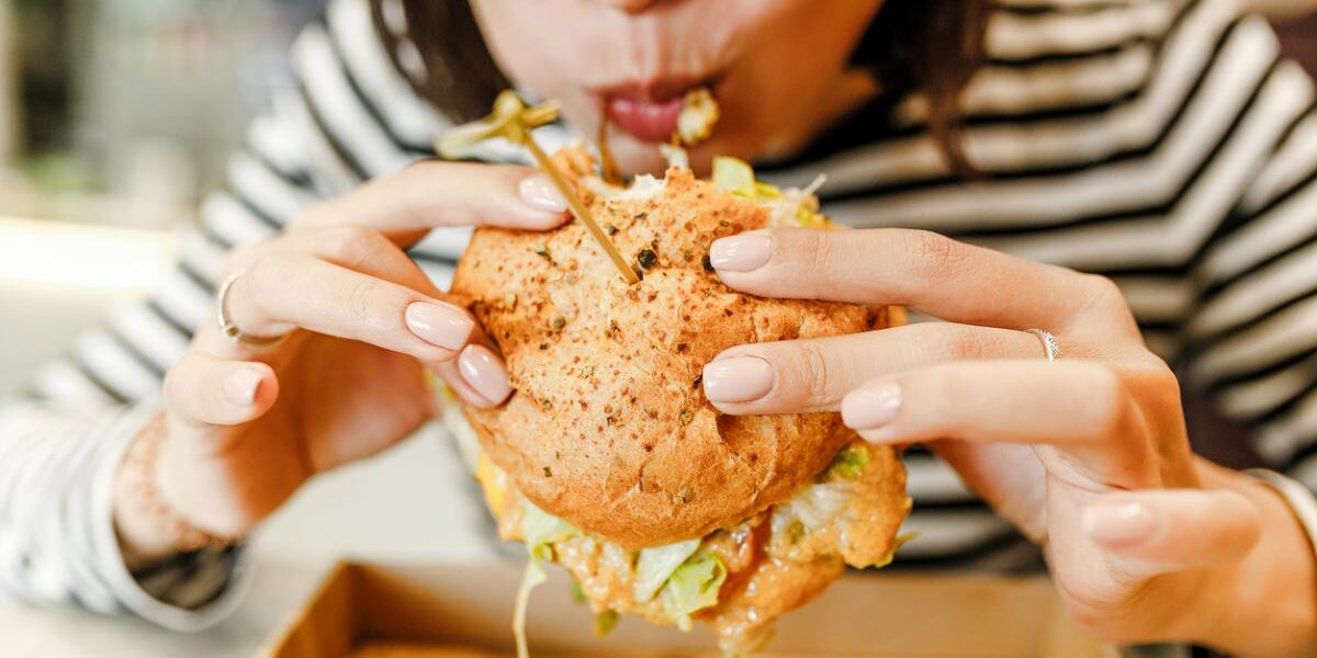 a woman biting into a burger in the United States, where life expectancy per country is lower than many European countries