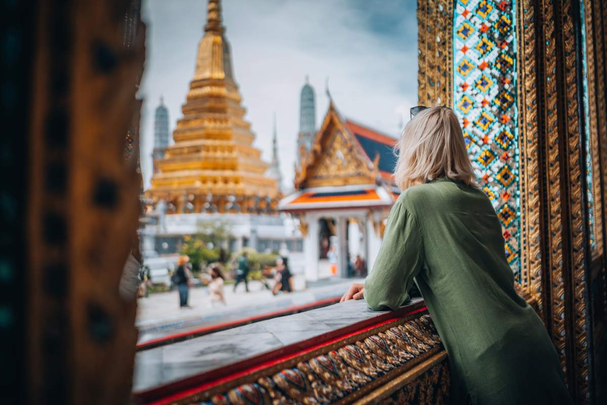 a woman looking out a window at the Grand Palace in Bangkok, where travel insurance for Thailand is advised