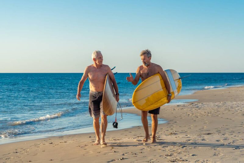 two men walking with surfboards on a beautiful beach in Australia, where the life expectancy per country is one of the highest in the world