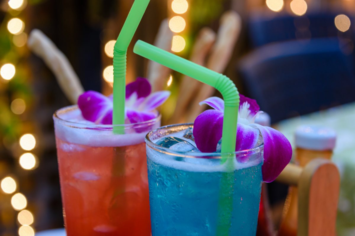 Red and blue cocktails with straws and purple flowers in a bar, indicating the need for travel insurance in Thailand in case of drink spiking