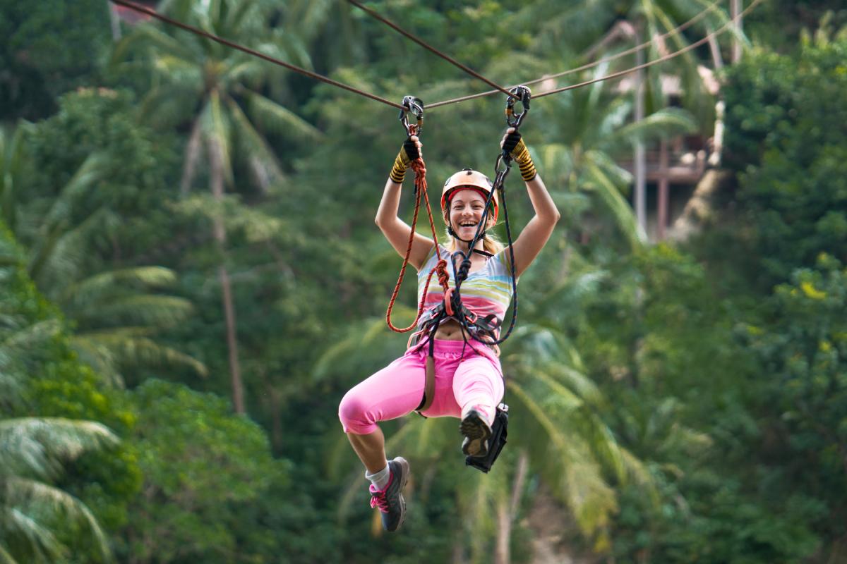 a woman ziplining in the rainforest, indicating the importance of having travel insurance for Thailand