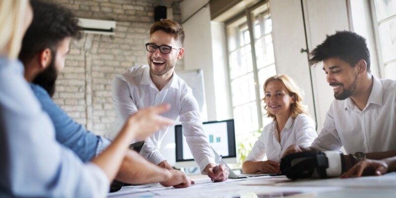 Group of people sitting around a table with a man talking.